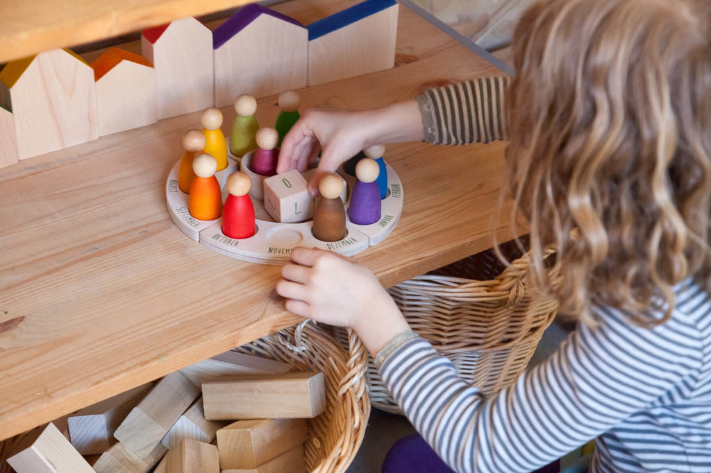 Bambina che sistema i Nins colorati sul calendario perpetuo Grapat per esplorare mesi e stagioni.