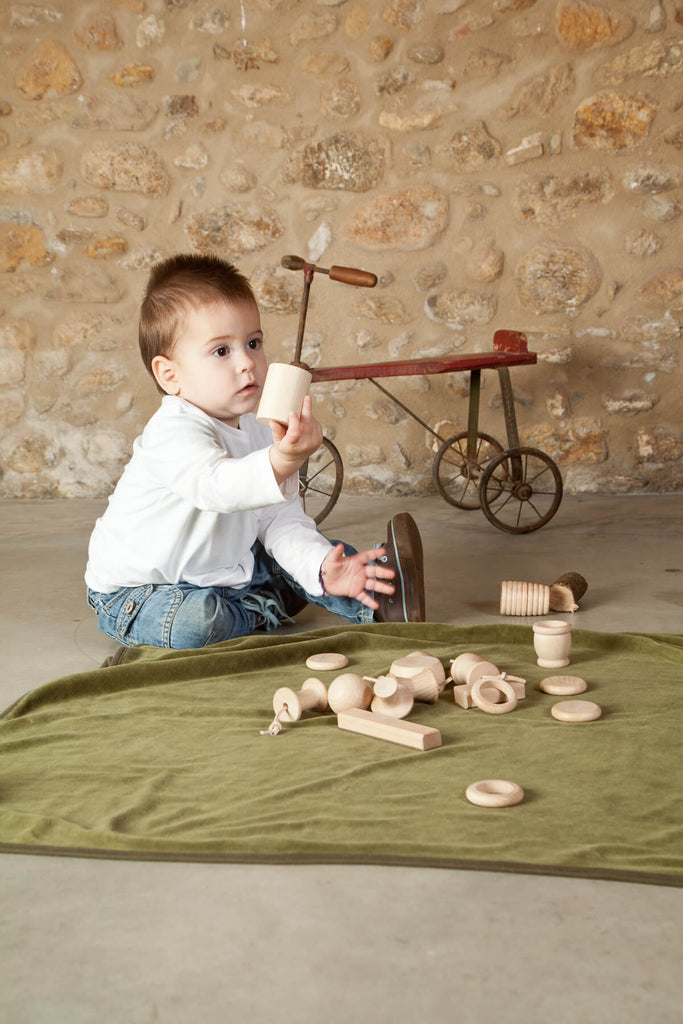 Bambino che osserva un elemento in legno del cestino dei tesori Grapat, attività di manipolazione e scoperta.