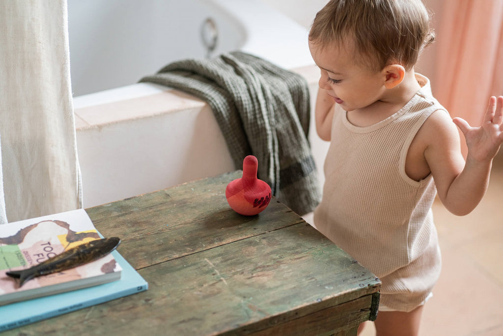 Bambino che osserva il Grapat Chill Pink Bird su un tavolino di legno, luce naturale calda