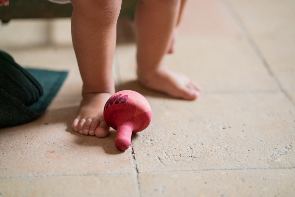 Dettaglio del Grapat Chill Pink Bird vicino ai piedi del bambino, colori naturali e texture del legno