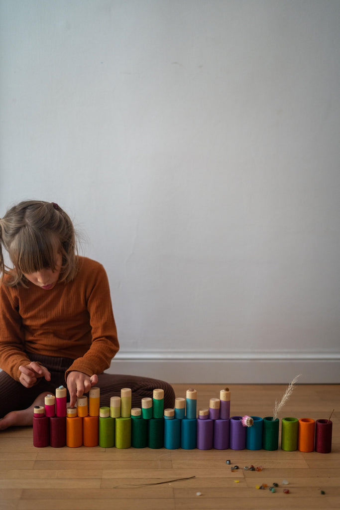 Cilindri colorati del set Grapat LA disposti in fila sul pavimento, gioco libero con materiali naturali