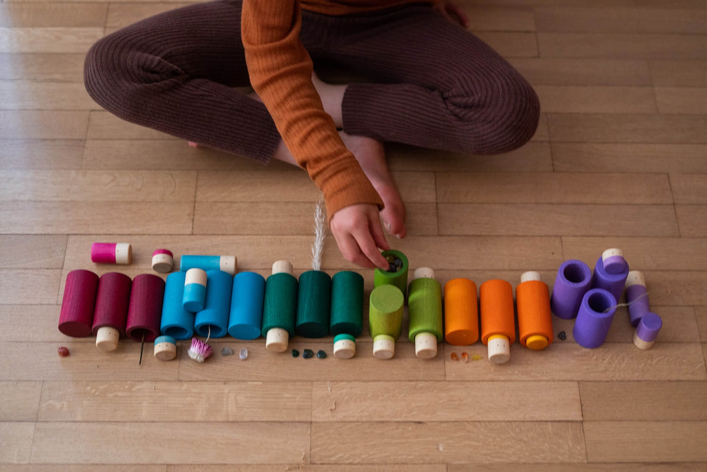 Bambino che inserisce piccoli oggetti nei cilindri colorati del set Grapat LA, attività di motricità fine e concentrazione