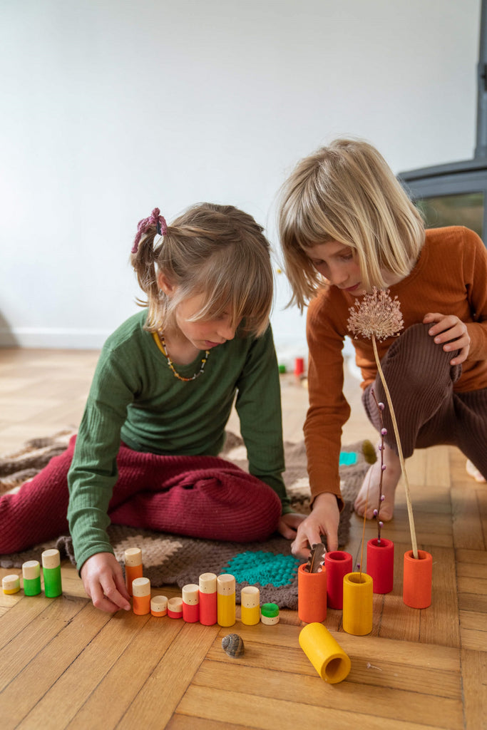 Due bambini che giocano insieme con il set Grapat LO, ordinando i cilindri colorati in legno