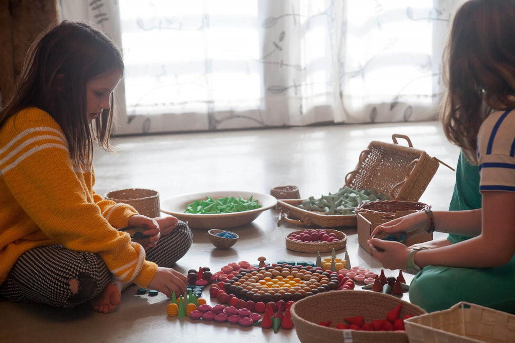Bambini che compongono un mandala con vari elementi Grapat, inclusi i fiori rosa del set Mandala Flowers Pink.