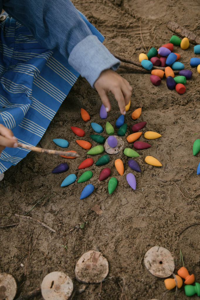Bambini che giocano all’aperto con i fiocchi di neve Grapat Mandala, creando composizioni colorate nella sabbia