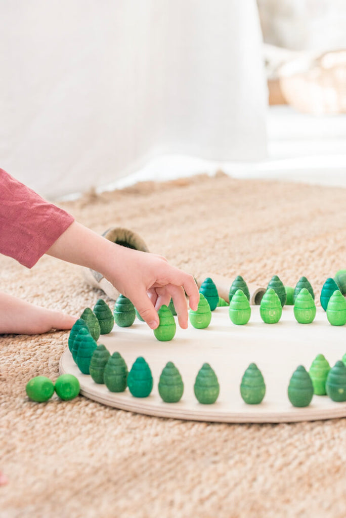 Dettaglio della mano di un bambino che dispone gli alberelli in legno del set Grapat Mandala Tree su una base rotonda