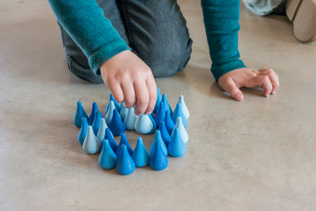 Bambino che gioca con le gocce blu Grapat Mandala Water Drops, creando composizioni sul pavimento