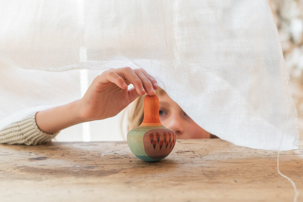 Bambina che osserva e tocca il Grapat Mellow Orange Bird dietro un velo bianco, gioco in legno colorato