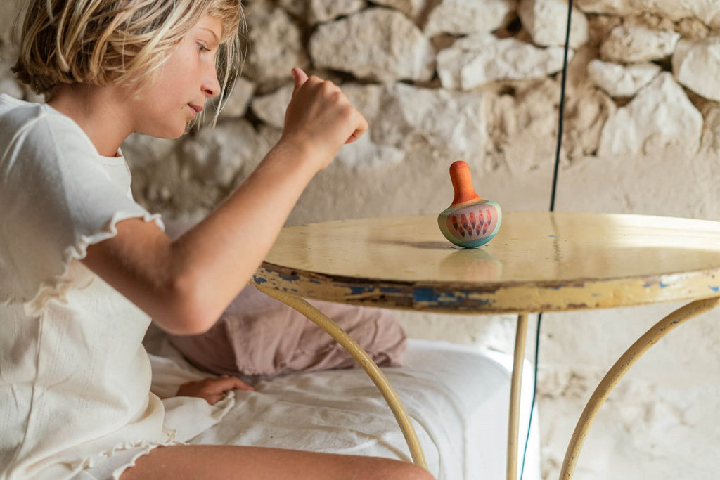 Bambina
 che fa girare il Grapat Mellow Orange Bird su un tavolino, luce naturale e sfondo in pietra