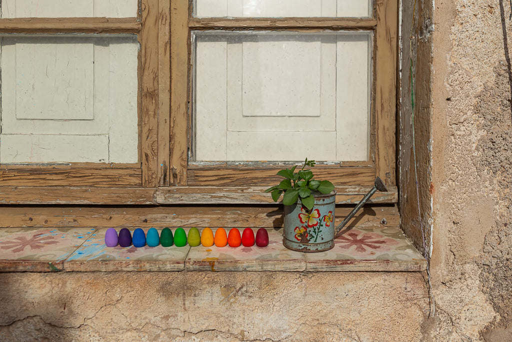Grapat Rainbow Eggs colorati allineati su un davanzale accanto a un piccolo annaffiatoio decorato