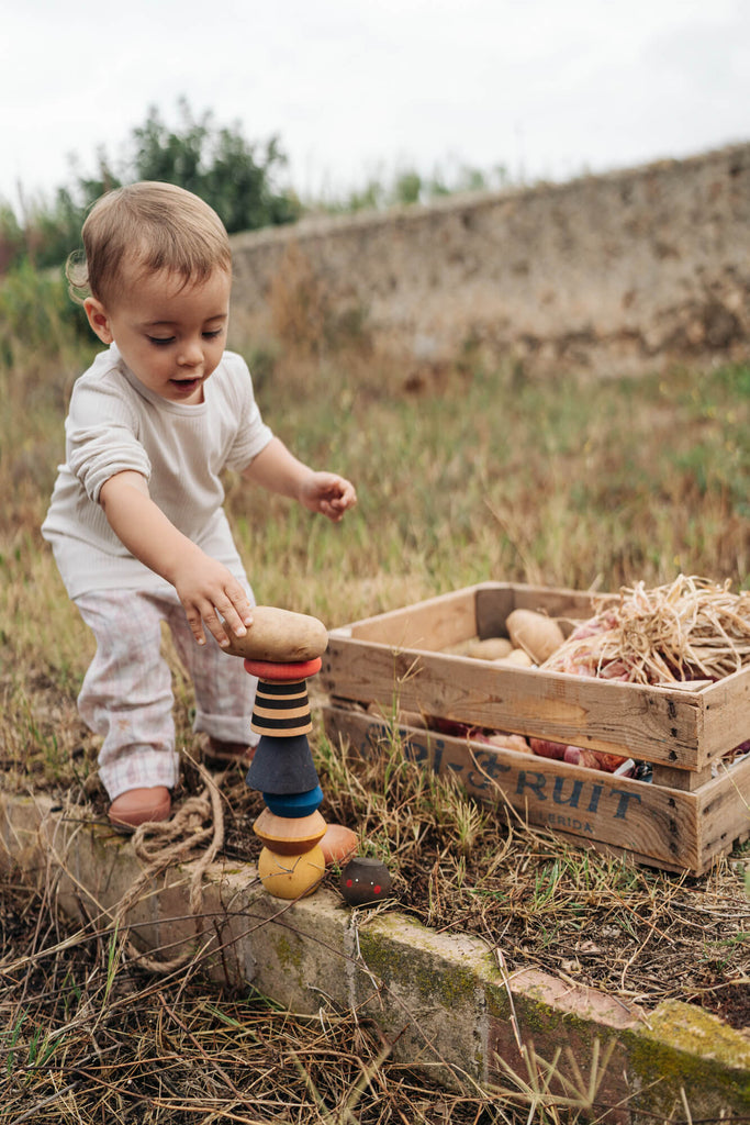 Bambino che gioca con il Grapat Serendipity all’aperto vicino a una cassetta di legno, materiali naturali.