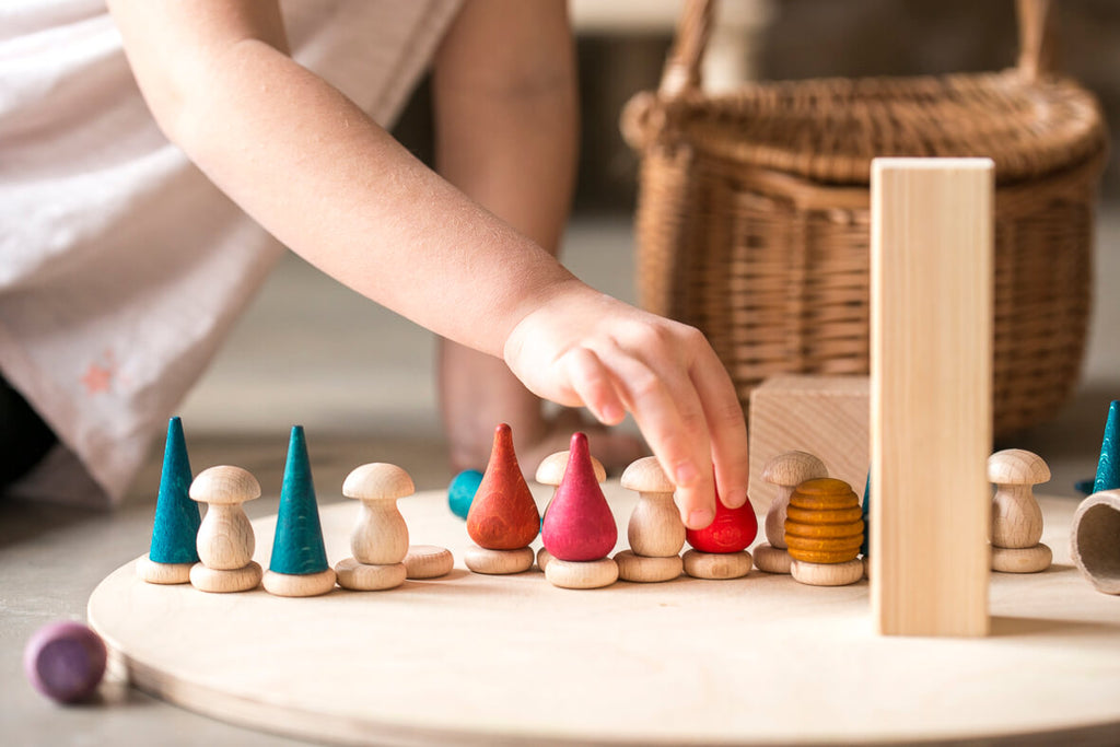 Mano di un bambino che dispone i Grapat Tomtens e gli elementi in legno (funghi, coni, gocce) su una base rotonda