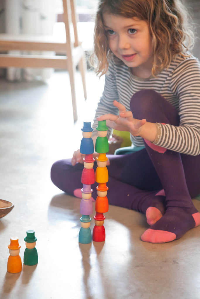 Bambina che impila i Wizards Grapat colorati, costruendo torri con i personaggi in legno.