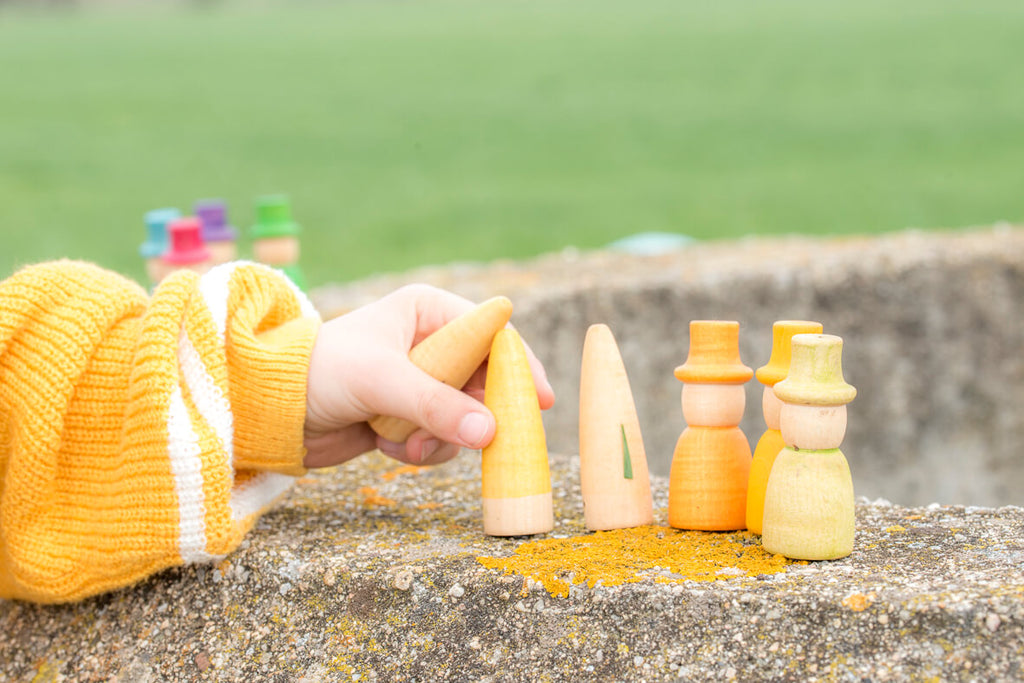 Mano di un bambino che gioca con alcuni Wizards Grapat gialli, appoggiati su un muretto all’aperto.